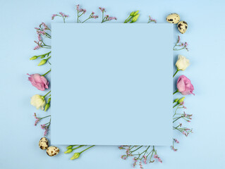 Easter composition. Easter eggs, flowers, paper blank on pastel blue background. Flat lay, top view, copy space, mock up.