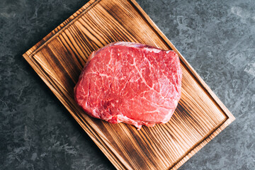 Raw beef steak on wooden board and black background.