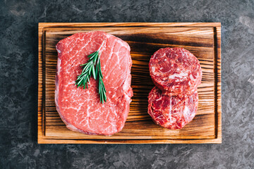 Raw beef steak and minced round steak for burgers on wooden board, top view .