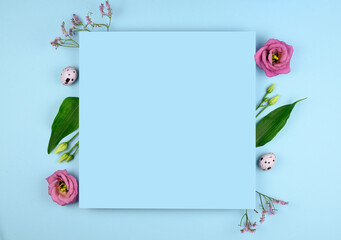 Easter composition. Easter eggs, flowers, paper blank on pastel blue background. Flat lay, top view, copy space, mock up.