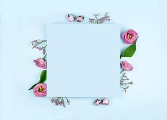 Easter composition. Easter eggs, flowers, paper blank on pastel blue background. Flat lay, top view, copy space, mock up.
