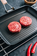 Fresh raw minced beef steak for burgers on black grill pan with chili pepper.