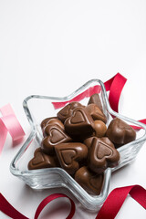 Valentines Day background with chocolates, hearts and red/pink ribbons in a star dish on white background