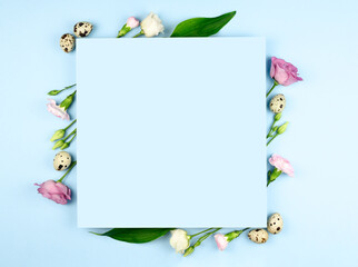 Easter composition. Easter eggs, flowers, paper blank on pastel blue background. Flat lay, top view, copy space, mock up.