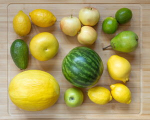 Flat composition of yellow and green fruits on light wooden board including melon, avocado, grapefruit, lemon, apple, lime, pear, quince, watermelon