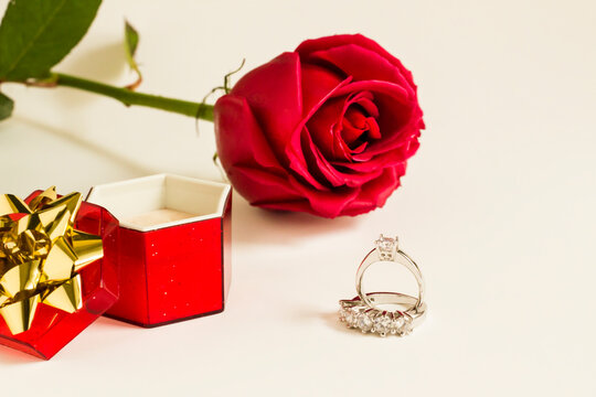 Five stone and single stone diamond,gold rings on white surface with red color ring box and fresh rose.Conceptual image.
