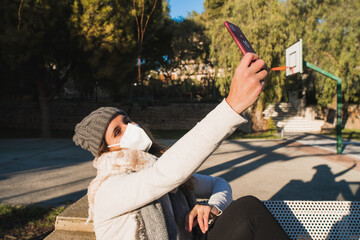 Young happy brunette woman with face mask making a selfie in the park at sunset.