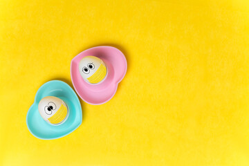 Eggs with funny faces in mask in a stand in the form of a heart on a yellow background.