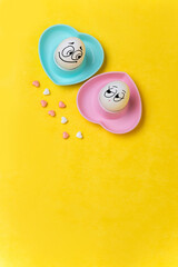 Eggs with funny faces in a stand in the form of a heart on a yellow background. Сandy in the form of hearts,  vertical banner