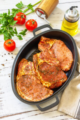Fresh raw pork loin on the bone with spices and marinade in a cast iron pan on wooden table, preparation for baking.