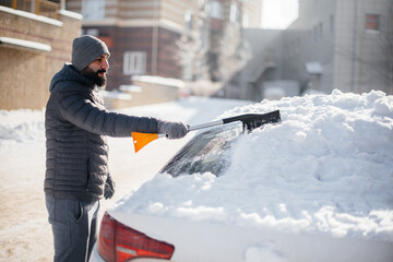 A young man cleans his car after a snowfall on a sunny, frosty day.