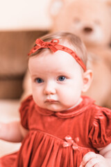 Very cute 7 months old toddler portrait. Beautiful little girl, posing naturally. Kid is wearing cute red dress and headband.