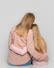 Shot of happy cheerful mom and daughter on gray background in studio, back view