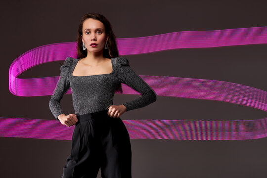 slim model against the backdrop of purple freezelight lines, attractive lady in dress posing isolated over dar studio background