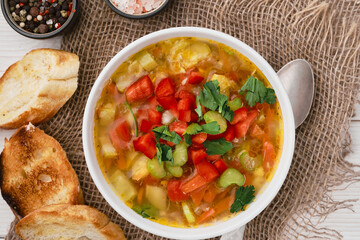 Minestrone soup in a white dish on burlap napkins, top view. Italian soup with seasonal vegetables, delicious healthy vegetarian food concept. Food diet idea. Flat lay