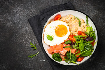 Savory breakfast. Oatmeal porrige with salted salmon, egg and fresh salad. Top view on black table.
