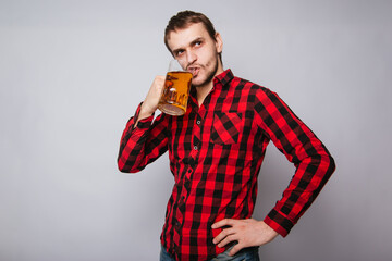 Young man in a checkered red shirt holding a large mug of beer without foam on a white background.