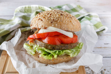 Healthy vegan tofu burger with spinach, lettuce, tomato, onion and fried vegetables