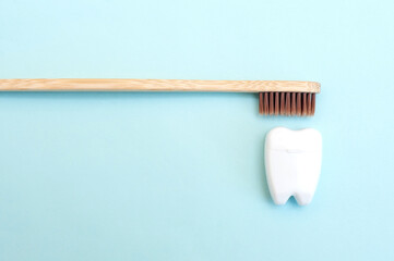 Fototapeta na wymiar Bamboo toothbrush and white dental floss in the form of a white tooth on a blue background.
