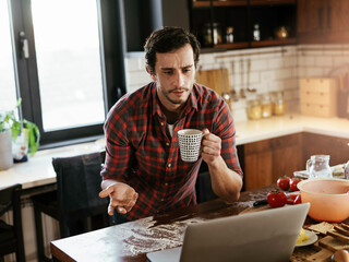 Young man drinking coffee and reading the news online. Handsome man enjoying at home..
