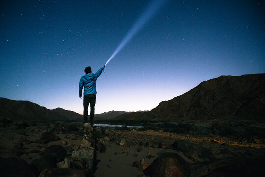 Hiker standing outdoors shining a torch beam into the stars - Powered by Adobe