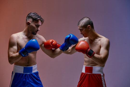 Wrestling of two fighting guys with fit torsos in boxing gloves in red light in studio, martial arts, mixed fight