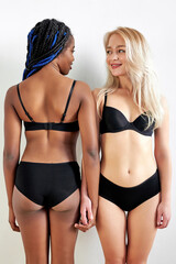 afro and caucasian women in underwear have flat belly stand closely to each other, posing together,...