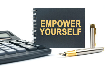 On a white background, there is a calculator, a pen and a black notebook with the inscription - EMPOWER YOURSELF