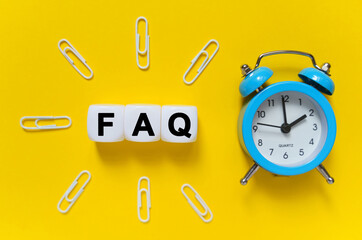 On a yellow background, a blue alarm clock, paper clips and white cubes on which the text is...