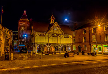 A view across the market square in Market Harborough, UK at night with a full moon in the background