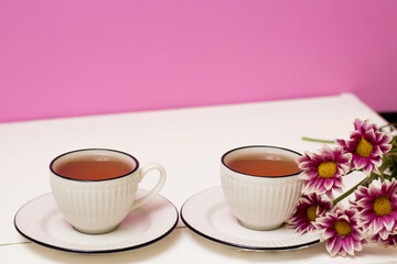 Fototapeta na wymiar Two cups of tea and pink chrysanthemums. Breakfast. Tea drinking. White wooden background. and pink background