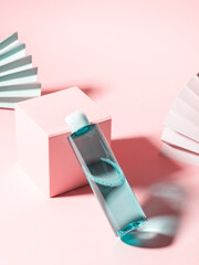 Blue facial skin care toner bottle on pastel pink geometrical background with podium and paper fans.