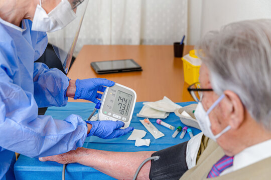 Nurse With Mask Taking Blood Pressure Of An Elderly Man