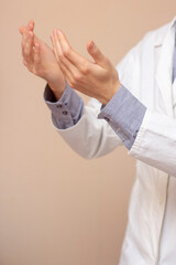 Obraz premium A young man in a white coat raised his hands up and pray. Beige background. Doctor praying. A Muslim makes dua.