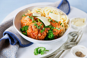 Meatballs with spaghetti, tomato sauce, parmesan cheese crumbles, broccolini, broccoli florets, vegan healthy dinner, lunch on light blue background. Close-up. selective focus.
