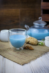 A glass cup and tea pot of blue Anchan Tea, cookies, milk,honey,almond.
