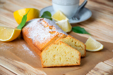 Moist lemon pound cake on parchment on rustic wooden background with slices of lemon and cup of tea on plate. Delicious breakfast, traditional tea time treat. Reciepe of American lemon pie loaf.