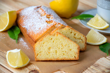 Loaf of gluten free lemon cake with sugar powder, pieces of lemon, green leaves  on rustic wooden background. Close up slice of citrus pie by classic recipe. Healthy nutrition, homemade vegan dessert.
