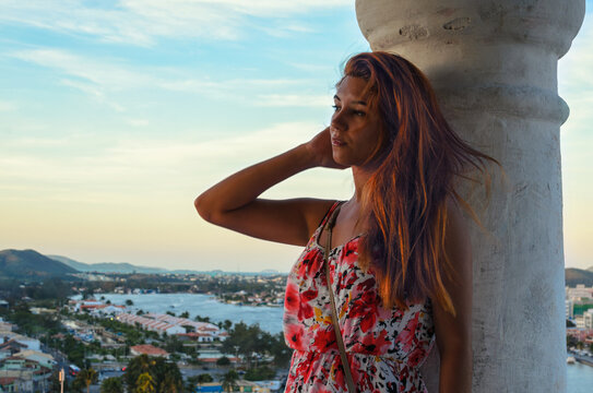 Redhead woman next to a column with aerial view to a coastal city