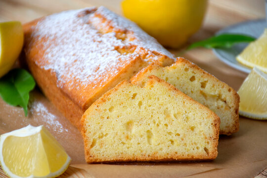 Loaf of gluten free lemon cake with sugar powder, pieces of lemon, green leaves  on rustic wooden background. Close up slice of citrus pie by classic recipe. Healthy nutrition, homemade vegan dessert.