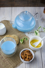 A glass cup and tea pot of blue Anchan Tea, cookies, milk,honey,almond.