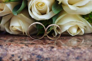Wedding rings on granite stand against the background of a beautiful bouquet of flowers