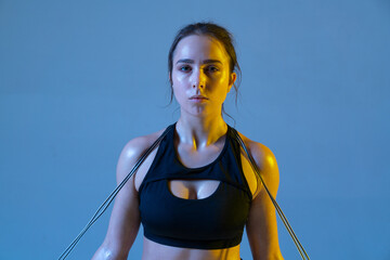 Serious athletic young woman looking camera and holding rope on her shoulders.