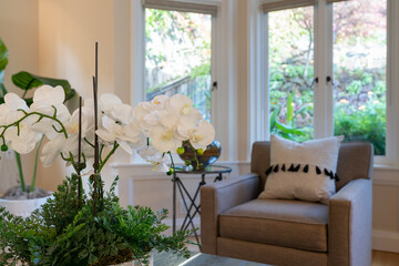 Detail of blooming orchid flowers near side chair and window view of garden. 