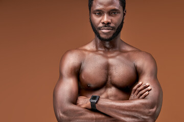 Fototapeta na wymiar african sportsman standing with crossed arms posing at camera, isolated on brown background. sport and bodybuilding concept