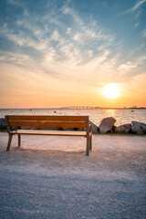 Isolated empty public bench at sunrise. Re island bridge in the background. portrait format