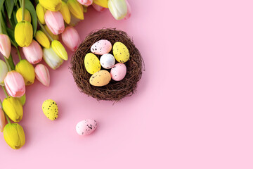Colorful easter quail eggs in nest and tulips on pink background with . Flat lay. Spring composition. Happy easter greeting card. Copy space