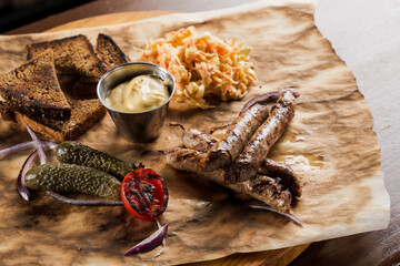Grilled sausages with beer and vegetables with pickled cucumber, cabbage salad sauce and bread on parchment, top view.