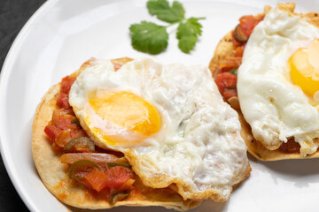 Fried eggs with sauce and tortilla called rancheros for  breakfast on dark background. Mexican food