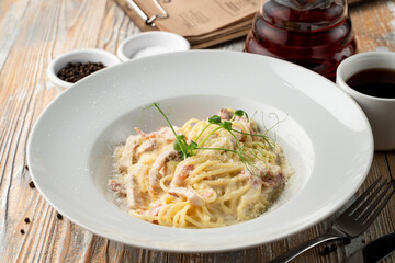 Carbonara creamy pasta with bacon crisps on a light wooden table in a restaurant